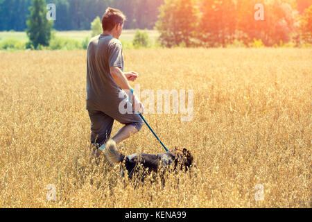 Man with dog on a leash running in an oat field in summer Stock Photo