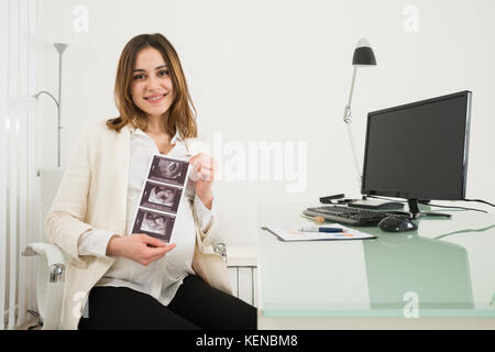 Happy Pregnant Businesswoman Holding Ultrasound Scan Reports In Office Stock Photo