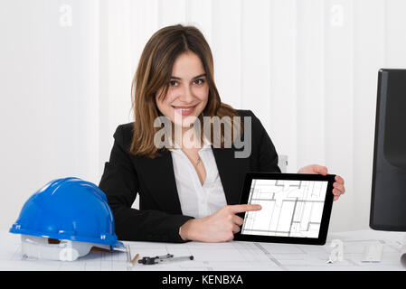 Happy Young Female Architect Pointing At Blueprint On Digital Tablet Stock Photo
