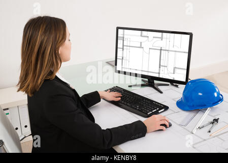 Young Female Architect Looking At Blueprint On Computer In Office Stock Photo