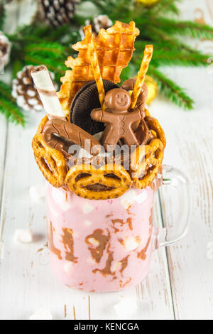 Freakshake from pink smoothie, cream. Monstershake with a chocolate, cane, pretzels, biscuits, waffles and marshmallow. Extreme milkshake in a Mason j Stock Photo