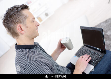 handsome businessman having cup of coffee while using laptop indoors Stock Photo