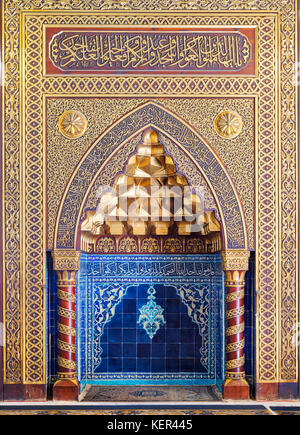 Golden ornate arched mihrab (niche) with floral pattern, blue Turkish ceramic tiles and arabic calligraphy at the public mosque of The Manial Palace o Stock Photo