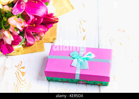 Gift in a box and a bouquet of flowers on a white wooden table. Birthday party. Stock Photo