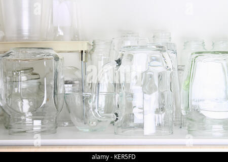Different glassware in a white closet on the shelf. Banks, jugs, glasses, mugs. Stock Photo