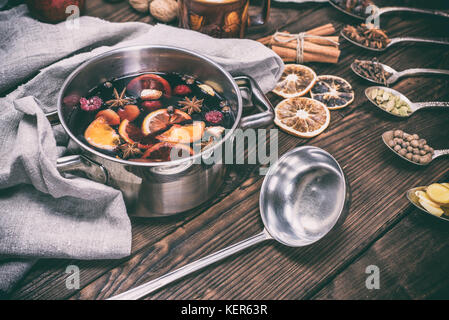 hot mulled wine in a pot with handles and an iron kitchen scoop on a brown wooden background, vintage toning Stock Photo