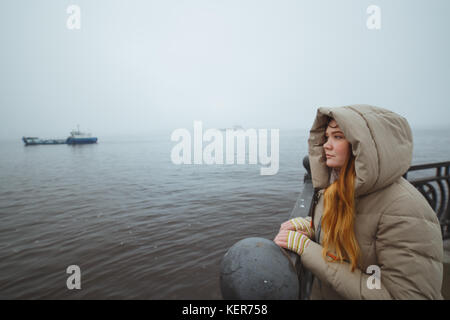 Woman standing alone at sea coast and looking on ship. Winter time. Seaman's wife. Stock Photo