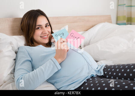 Happy Young Pregnant Woman Holding Paper With Girl And Boy Written On It Stock Photo