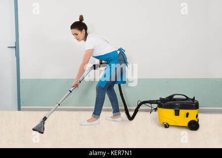 High Angle View Of Young Female Janitor Vacuuming Floor Stock Photo