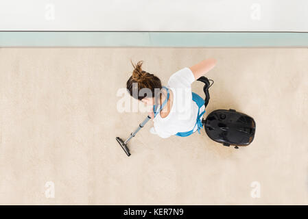 Young Female Janitor In Uniform Vacuuming Floor Stock Photo