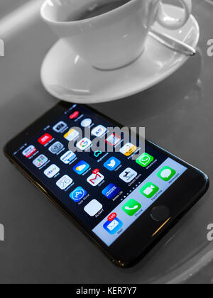 iPhone smartphone connect lifestyle coffee screen with apps icons on modern cafe table with variety of UK screen applications displayed WiFi connected Stock Photo