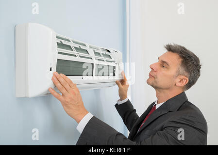 Mature Businessman Checking Air Conditioner In Office Stock Photo