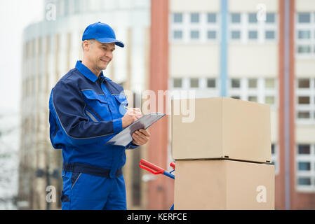 Portrait Of Confident Delivery Man With Parcels And Clipboard Against Truck Stock Photo