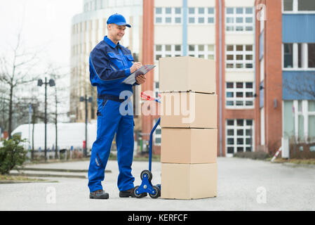 Portrait Of Confident Delivery Man With Parcels And Clipboard Against Truck Stock Photo