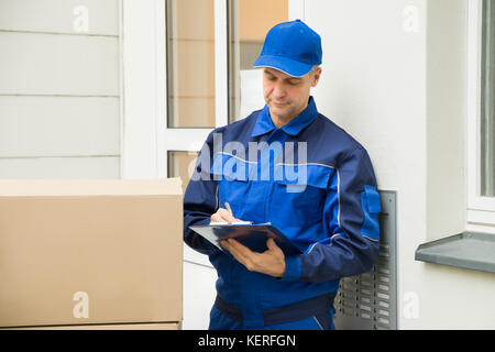 Delivery Man With Cardboard Boxes Writing On Clipboard Stock Photo