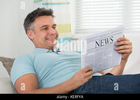 Mature Happy Man Reading Newspaper Lying On Sofa Stock Photo