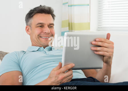 Mature Happy Man Lying On Sofa Using Digital Tablet Stock Photo