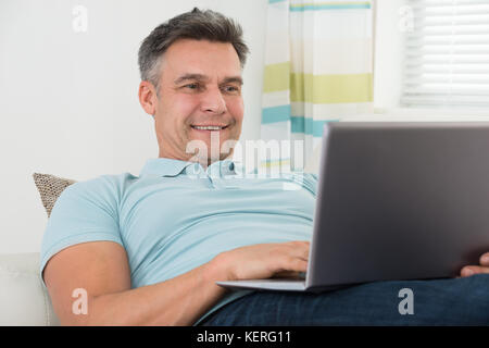 Mature Happy Man Lying On Sofa Using Laptop Stock Photo