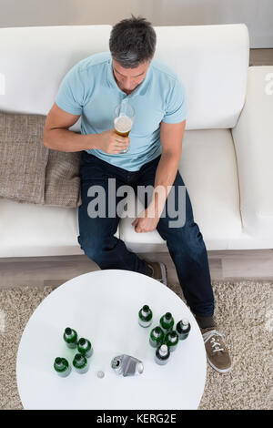 Mature Man Sitting On Sofa Holding Glass Full Of Beer At Home Stock Photo