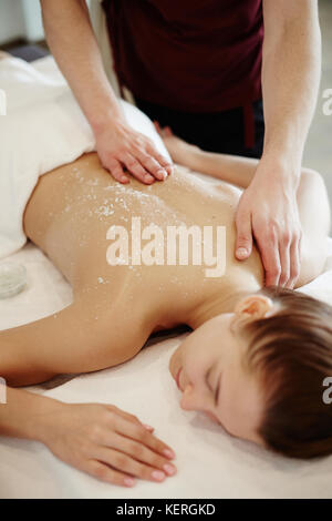 Closeup of unrecognizable male masseur rubbing back of young woman lying on massage table with eyes closed Stock Photo