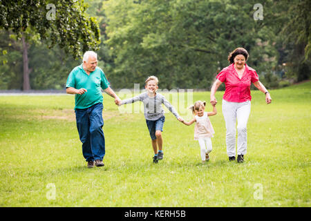 Happy Senior Grandparents And Grandchildren Running In The Park Stock Photo