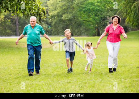 Happy Multigeneration Family Of Grandparents And Grandchildren Running In The Park Stock Photo