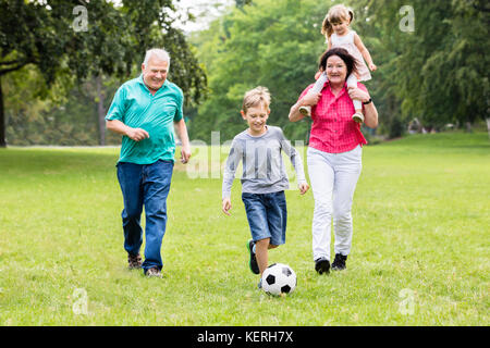 Happy Family Playing Soccer Game Together Running For Ball Stock Photo