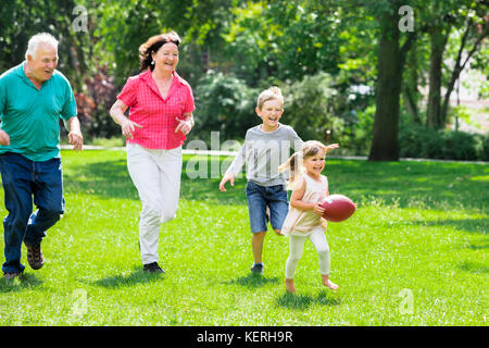 Happy Family Having Fun Playing With Rugby Ball In Park Stock Photo