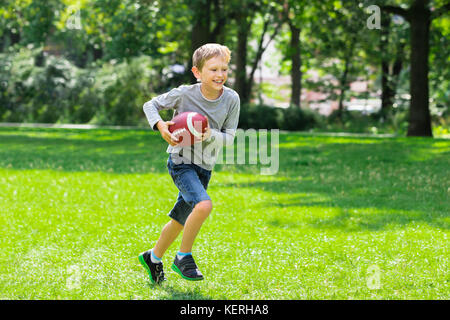 Boy Having Fun Running With Rugby Ball In The Park Stock Photo