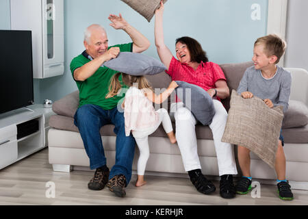 Grandparent And Kids Having Pillow Fight While Sitting On Couch Together At Home Stock Photo