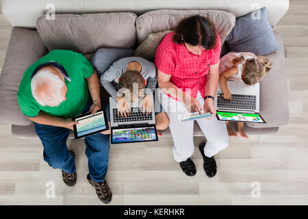 High Angle View Of Family Using Laptop Computers And Tablet On Couch At Home Stock Photo