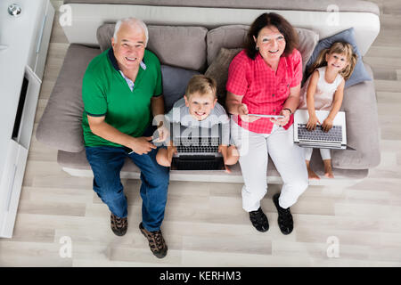 Family With Kids Using Laptop Computers And Tablets On Couch At Home Stock Photo