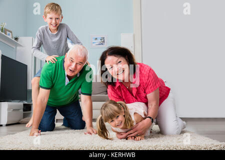 Happy Grandparents And Grandchildren Playing And Cuddling While Lying On Carpet In Living Room Stock Photo