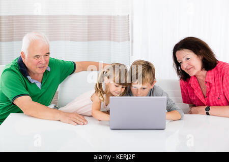 Smiling Kids Using Laptop Computer With Happy Family At Home Stock Photo