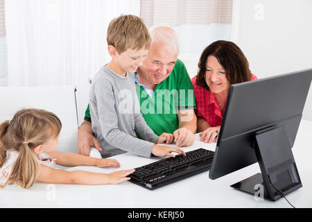 Happy Family With Smiling Kids Using Desktop Computer Together At Home Stock Photo