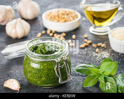 Homemade pesto sauce and ingredients on dark cement background. Close up wiev of basil pesto in glass jar with ingredients. Stock Photo
