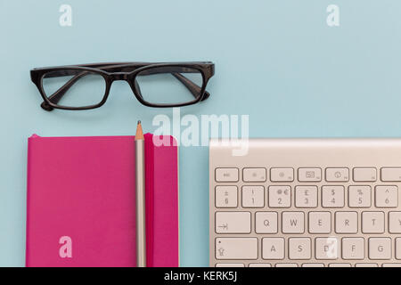 Computer keyboard, reading glasses and notebook on blue background Stock Photo