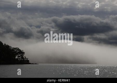 Huge fog bank rolling in from the Haro Strait, above San Juan Island, Washington State. Billowing dark clouds above, sea, silhouetted tip of island. Stock Photo