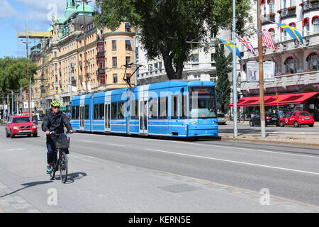 View of the roadway in the center of the city. Road traffic. A modern tram in the stream of cars. An elderly male cyclist on a bicycle is riding... Stock Photo