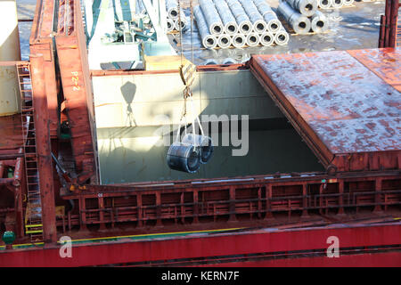 Loading huge aluminium coils as raw materials for heavy industry, instrumentation and engineering to the hold on the trading ship with a crane Stock Photo