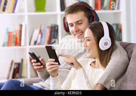 Happy couple listening to music on line with their smart phones sitting on a sofa at home Stock Photo