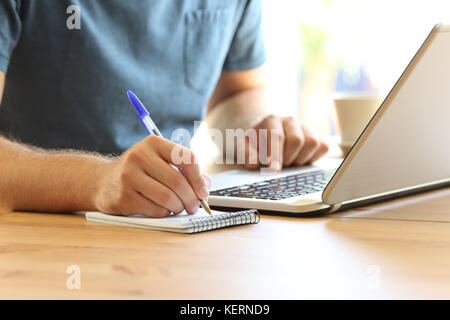 Close up of a man hand on line taking notes in a notebook and a laptop on a desktop Stock Photo