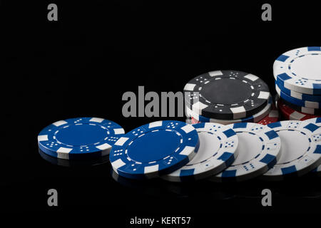 poker chips of different colors, scattered in length on a black reflective surface Stock Photo