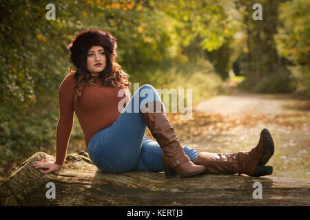 Beautiful woman sitting on a log in the autumn sunshine Stock Photo