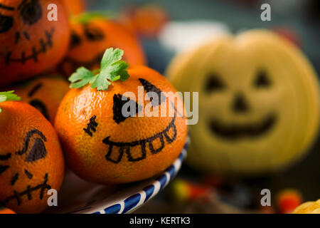 closeup of some tangerines ornamented as carved pumpkins with funny faces, a cookie in the shape of a carved pumpkin and some candies on a table Stock Photo