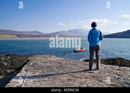 Cape Wrath Ferry, Sutherland. Visitor stands on slipway looking over Kyle of Durness to Beinn Spionnaidh, as ferryman goes to collect more passengers. Stock Photo