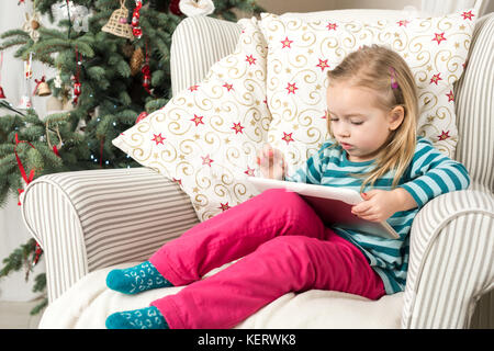 Girl playing with tablet PC near Christmas tree Stock Photo