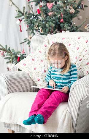 Girl playing with tablet PC near Christmas tree Stock Photo