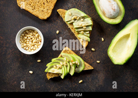 Sandwich avocado with fresh sliced avocado and pine nuts on a dark slate or stone background. Flat lay, top view. Stock Photo