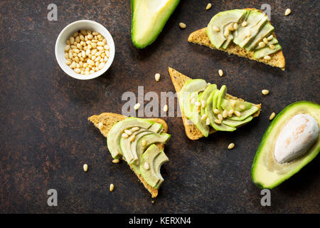 Sandwich avocado with fresh sliced avocado and pine nuts on a dark slate or stone background. Flat lay, top view. Stock Photo